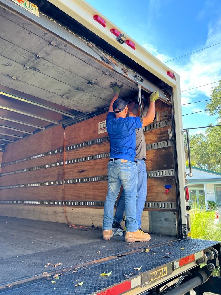 Two men are working on the back of a truck.
