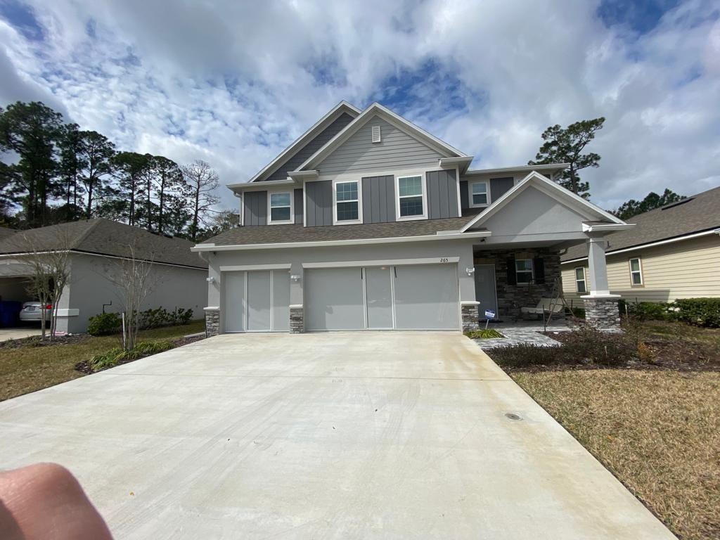 A person is standing in front of a large house with a concrete driveway.