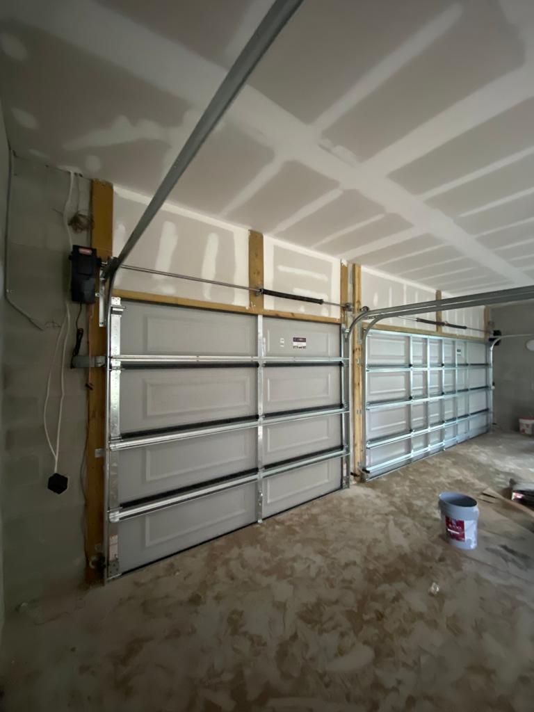 A garage with a garage door open and a bucket of paint on the floor.