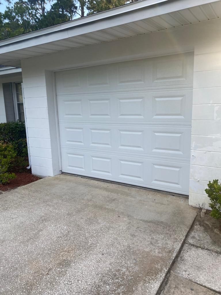 A white garage door is sitting in front of a white house.