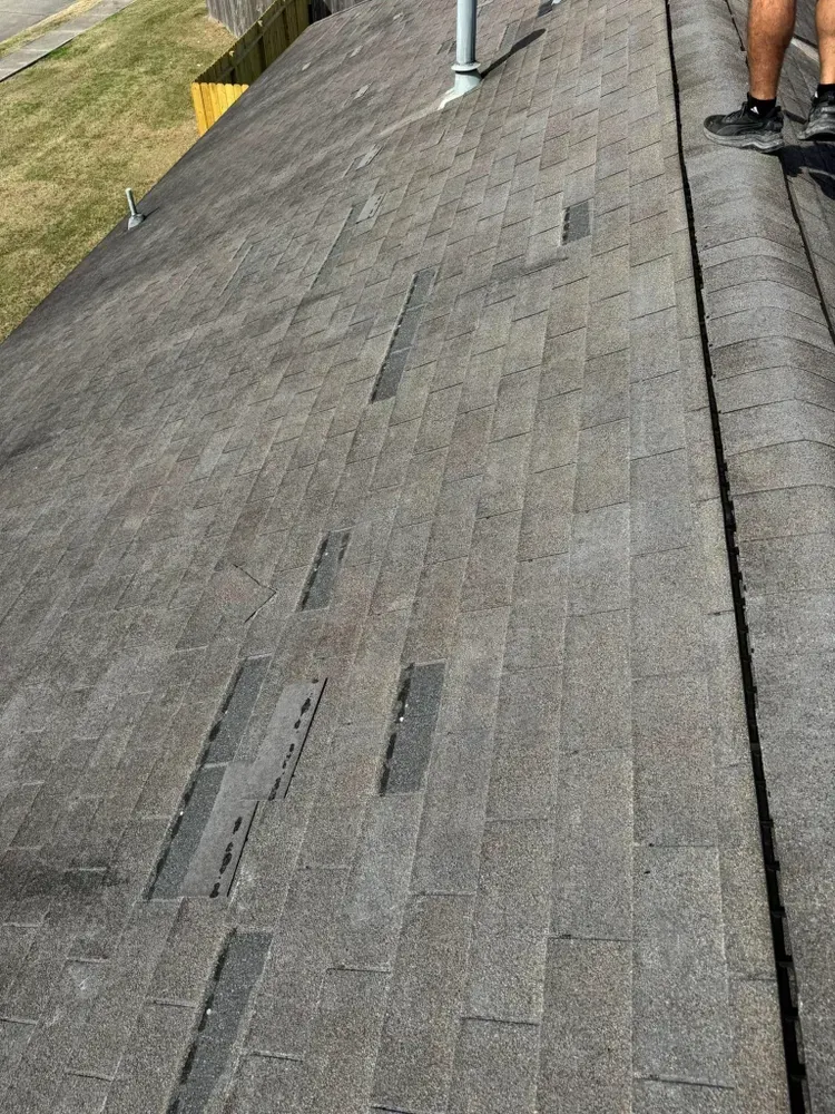 Gray asphalt shingle roof with several missing and damaged shingles on a sunny day.
