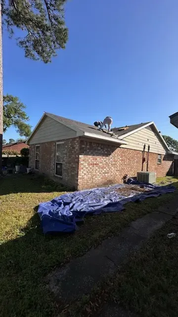 Brick house with damaged roof covered by blue tarp on a sunny day.