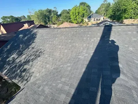 Overhead view of a gray shingle roof on a sunny day, with a person's shadow visible.