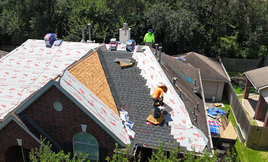 Roofers installing shingles on a house; workers on roof with supplies; partial roof replacement.