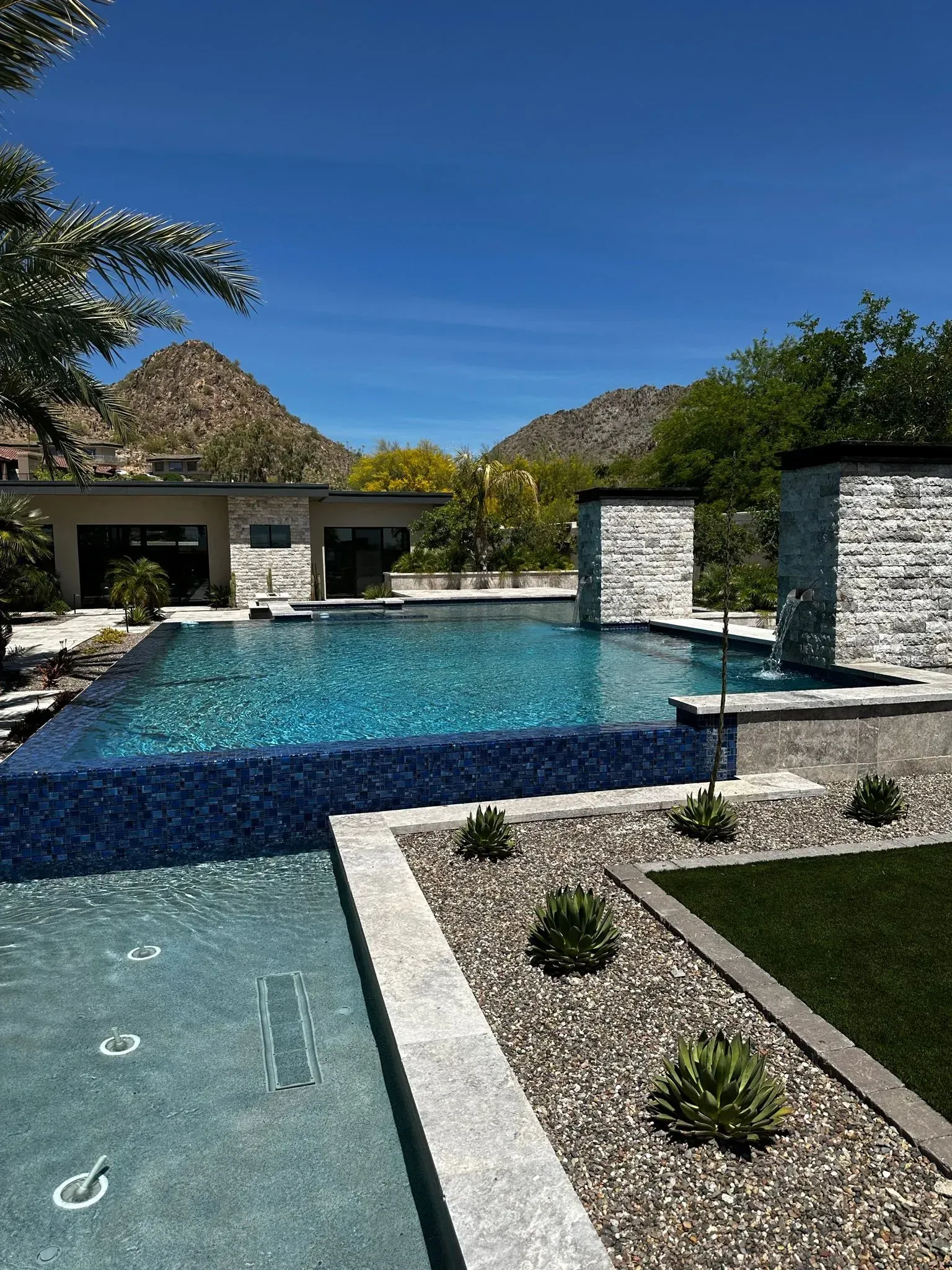 Luxury pool with blue tile surrounded by landscaping, with mountain backdrop.