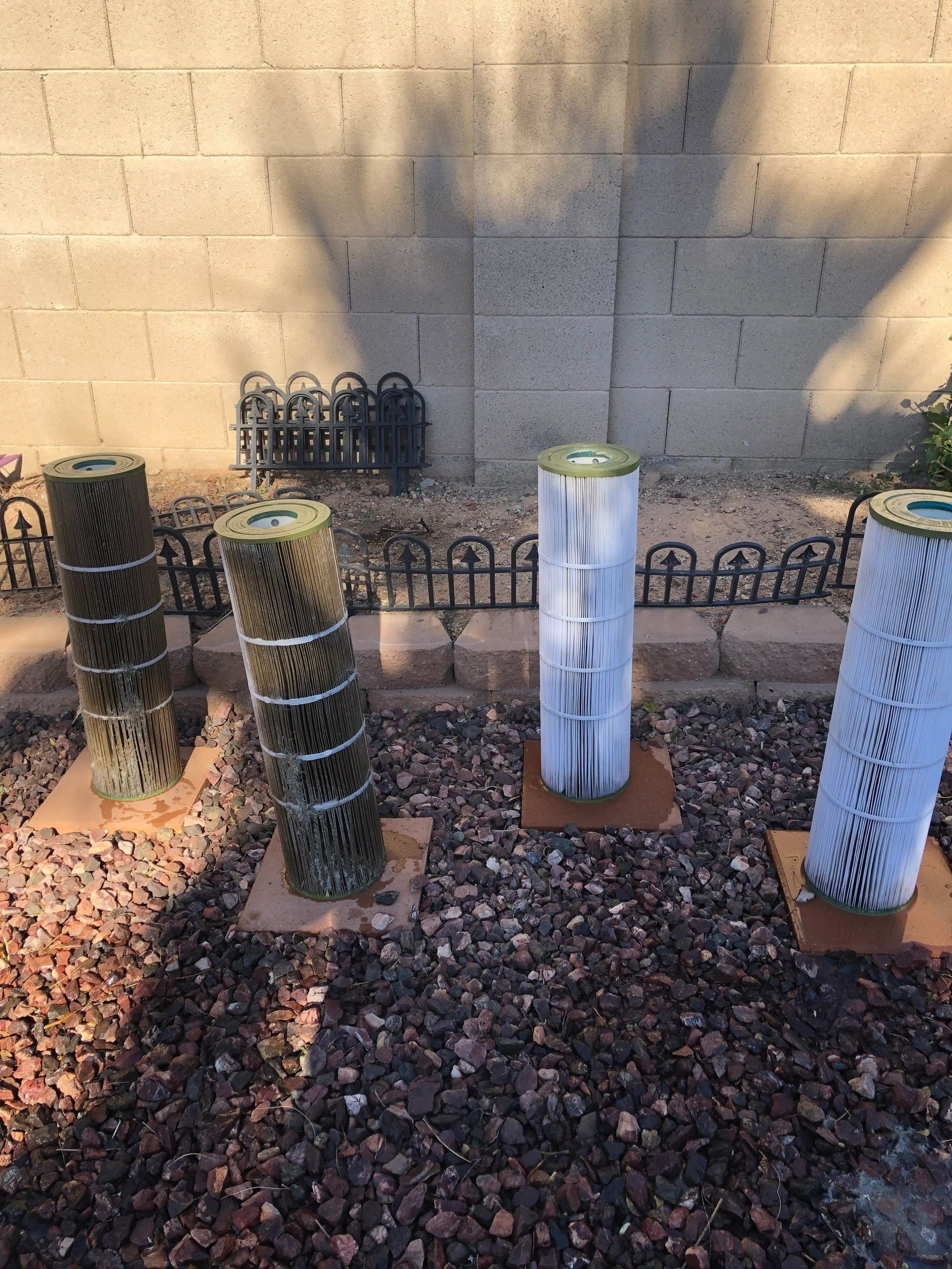 Four cylindrical pool filters standing upright on brown cardboard bases in a gravel bed.