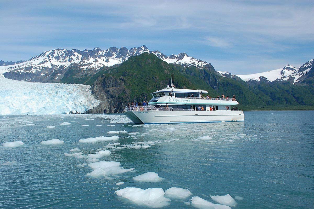 White tour boat sailing near glacier and mountains in Alaska.