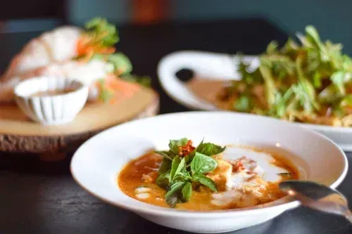 A table with three Thai dishes: soup, spring rolls, and fried vegetables.