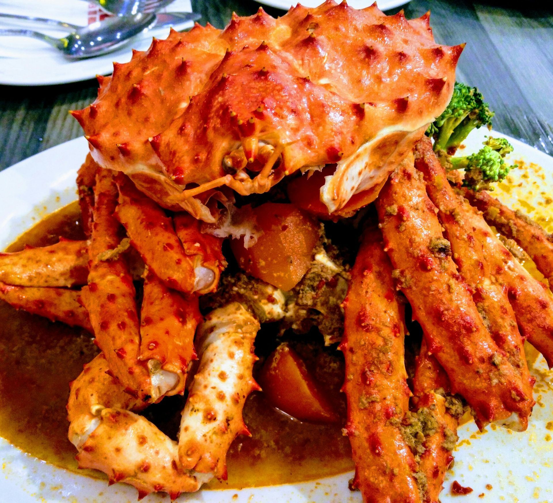 Cooked king crab on a white plate with sauce, crab legs extended, broccoli, and potatoes.