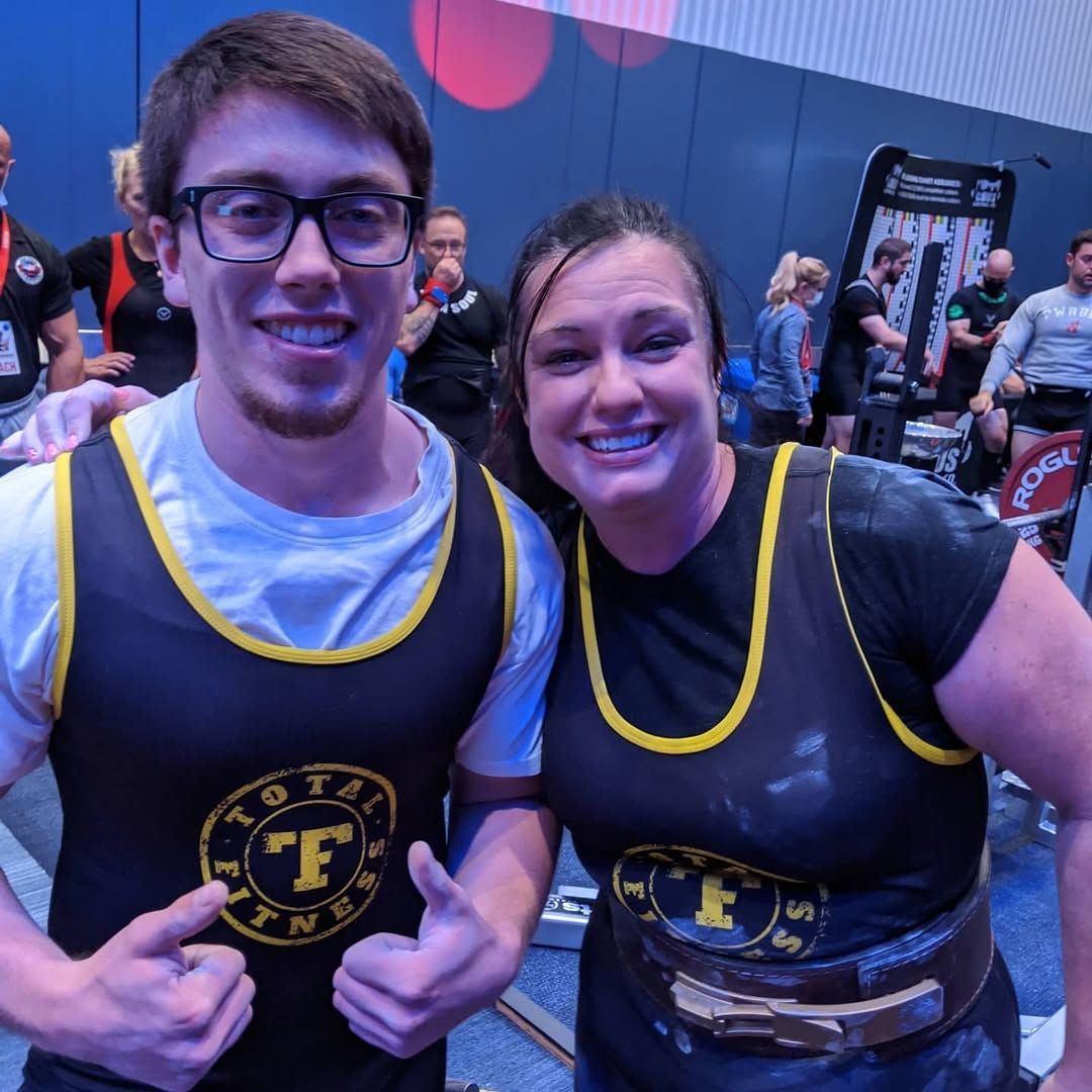 A man and a woman are posing for a picture and the man 's shirt says tf fitness