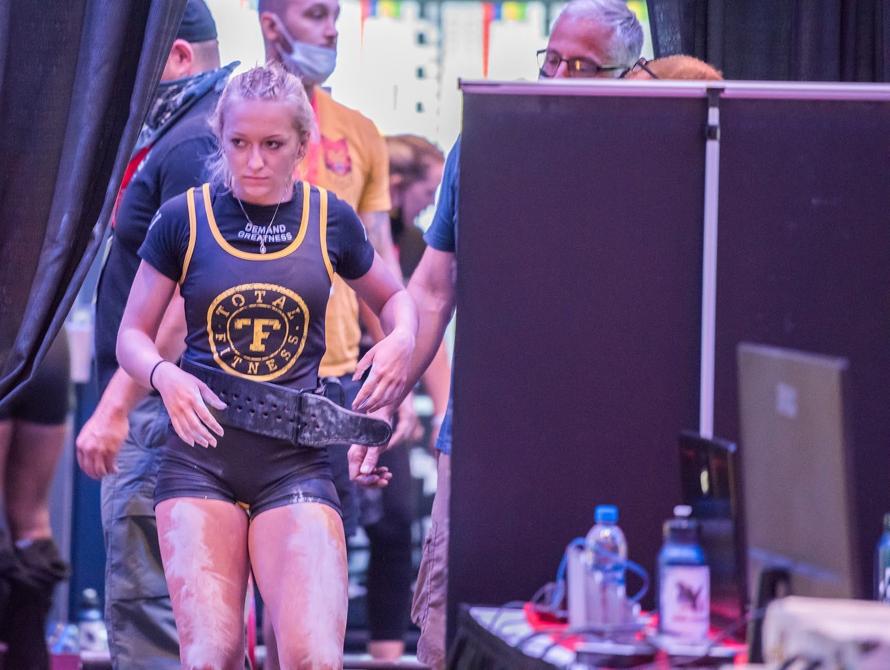 A woman in a black tank top with the letter f on it is walking on a stage.