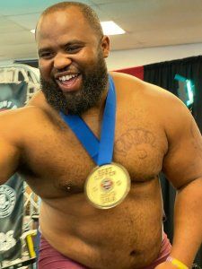 A shirtless man with a beard is wearing a medal around his neck.