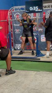 A man is squatting on a barbell in a gym.