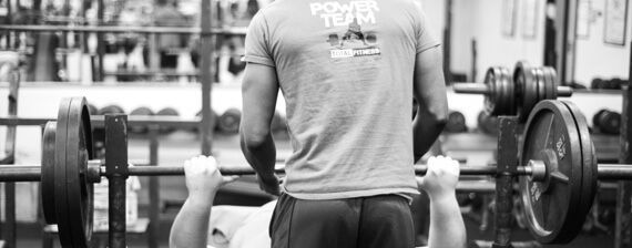 A man is lifting a barbell on a bench in a gym.