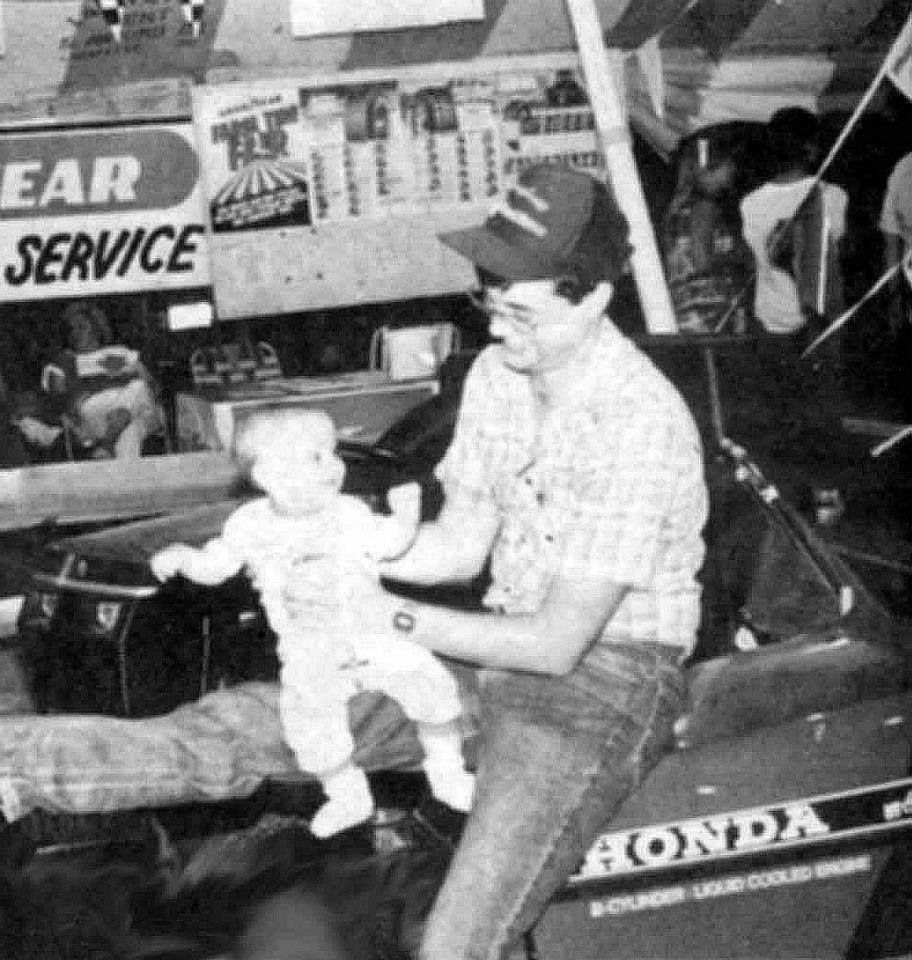 Man holding a baby near a Honda motorcycle. They are outdoors, possibly at an event.
