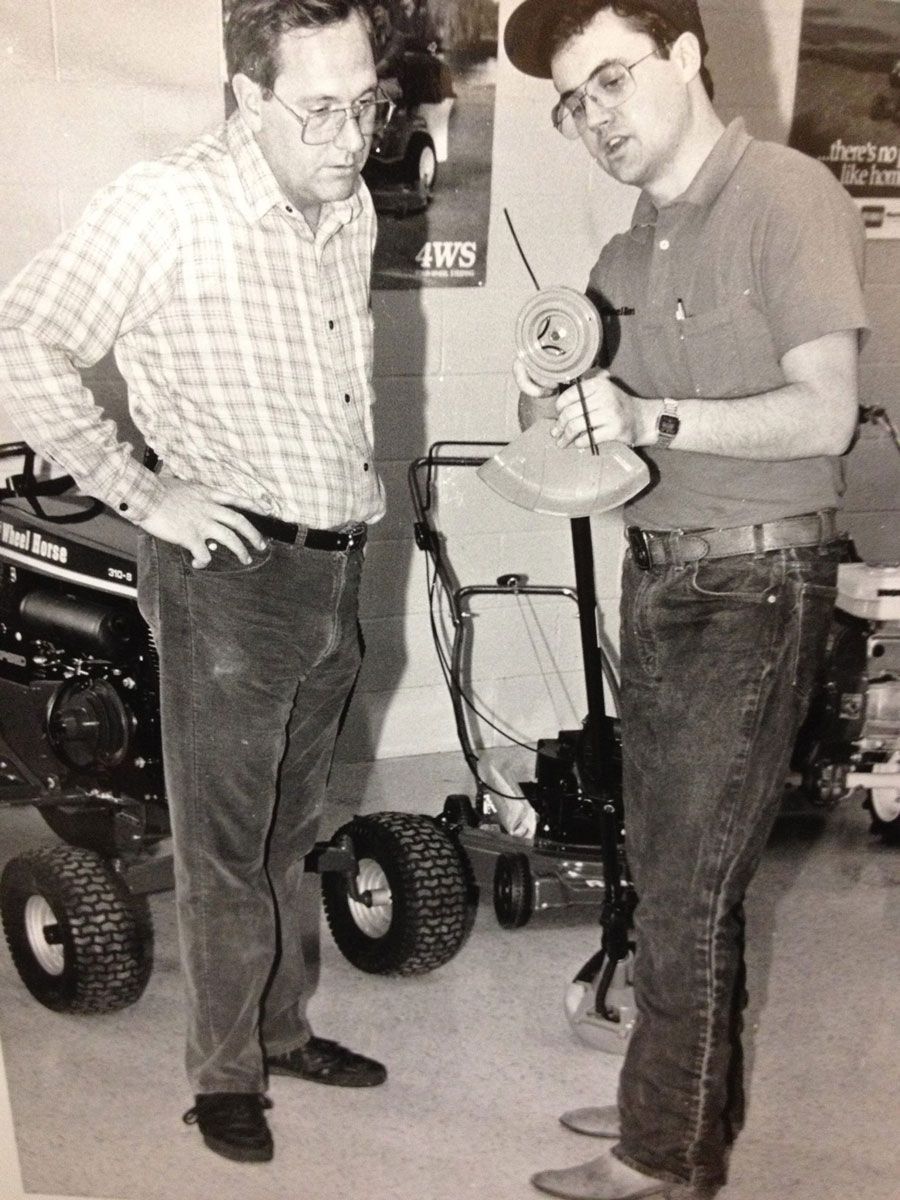 Two men examining a weed eater in a lawn equipment store.