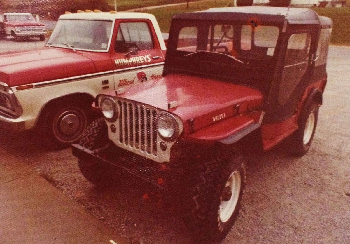 Red Jeep next to a red and white truck. Jeep has a black top. Both vehicles are parked.