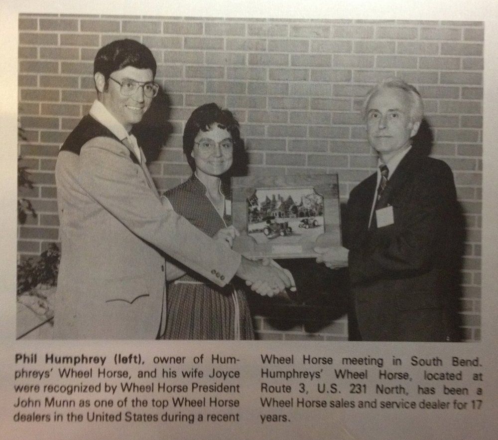 Three people in suits holding a framed picture; awarded to a Wheel Horse dealer for 17 years.