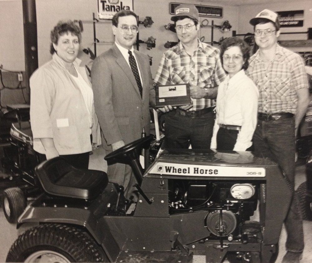 Group of five people posing with a Wheel Horse lawn tractor inside a store.
