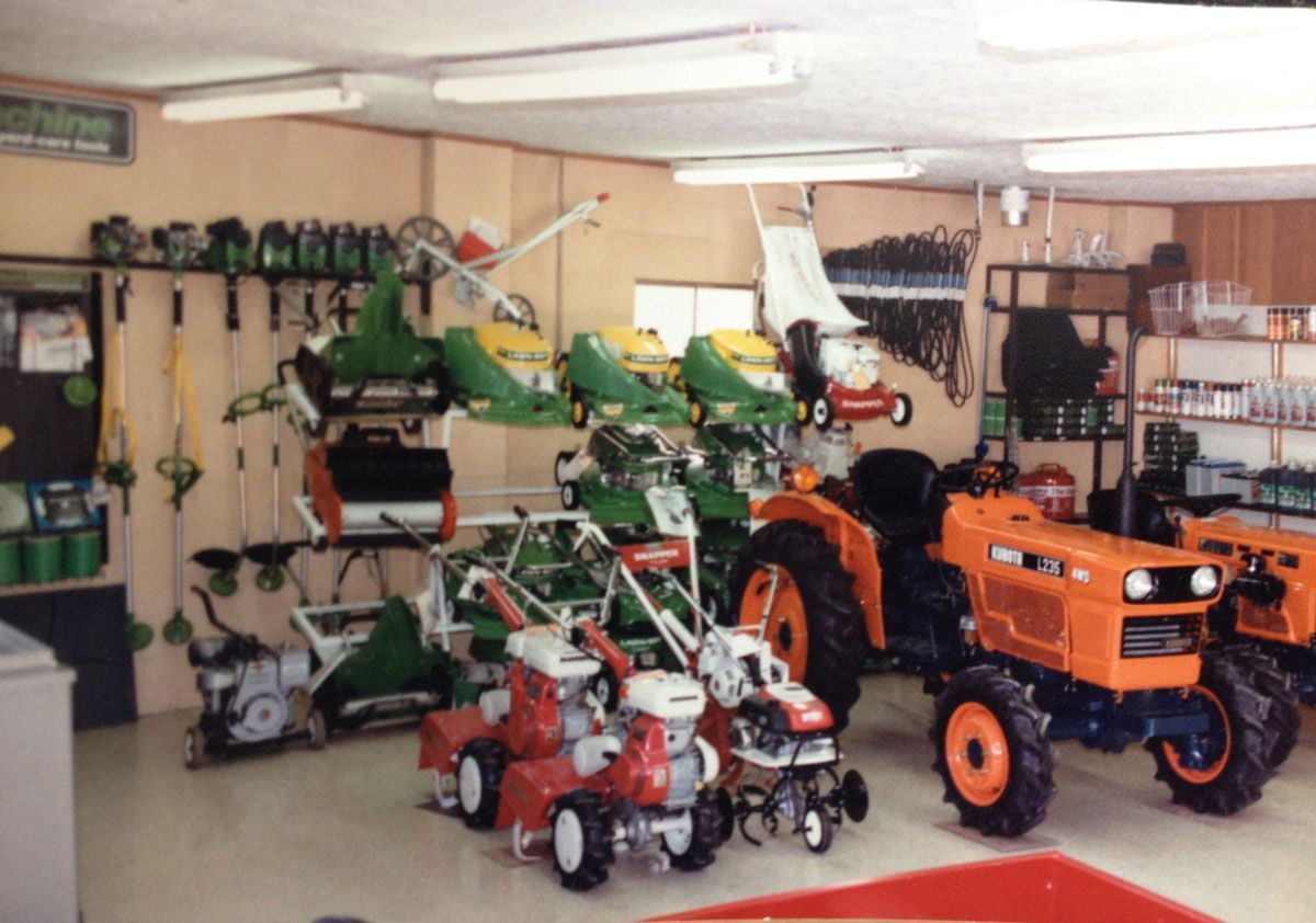 Inside a hardware store, various lawn care equipment is on display, including tractors and lawnmowers.