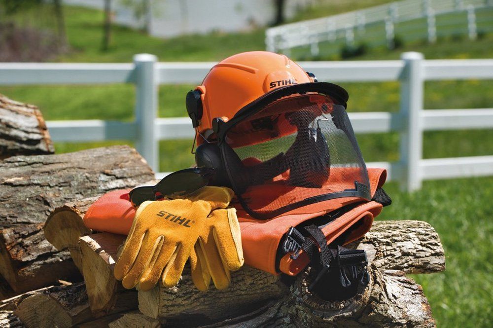 Orange forestry helmet, gloves, and protective gear on a pile of wood, outdoors.