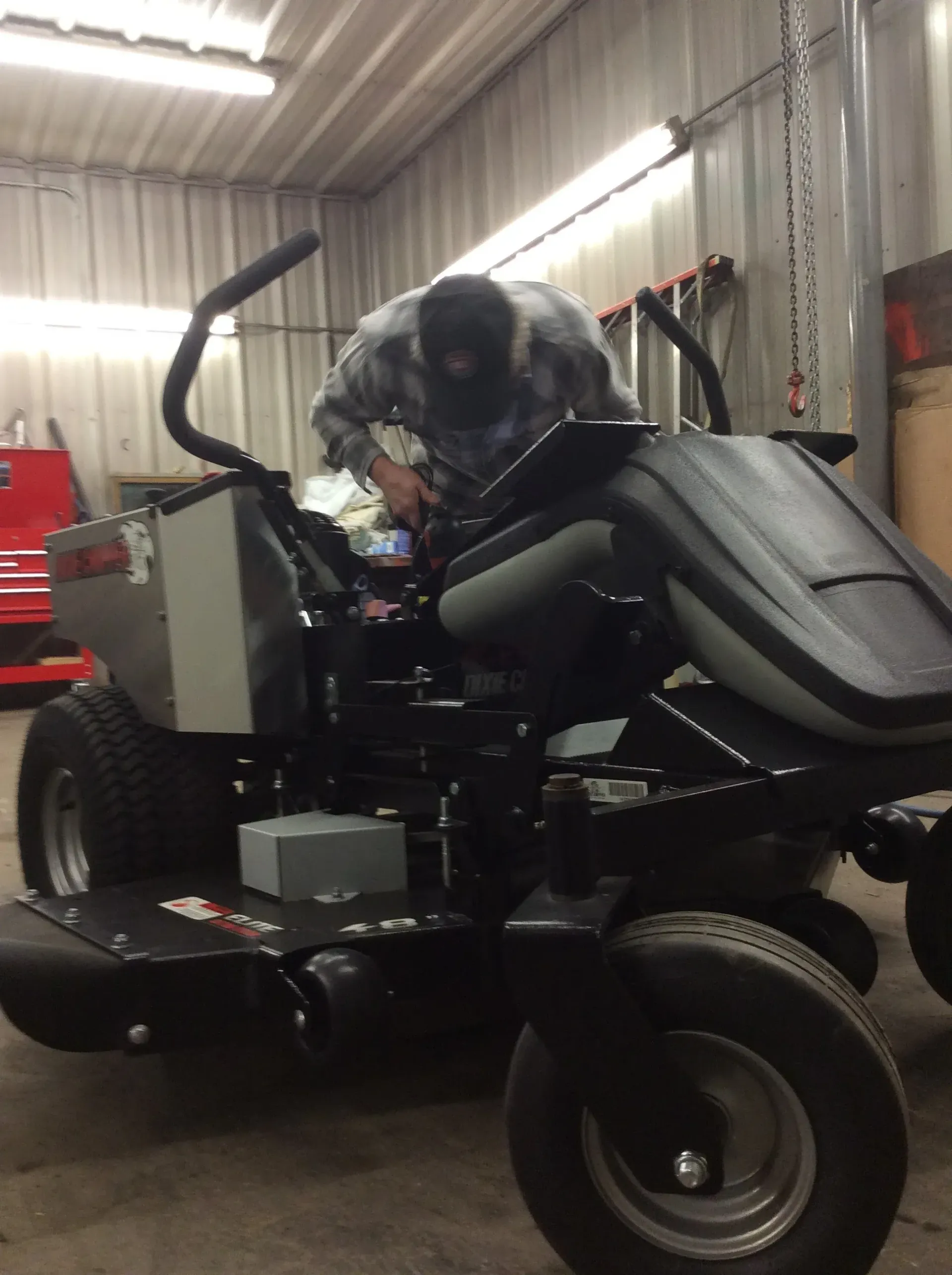 Man working on a black zero-turn mower in a garage, using tools.