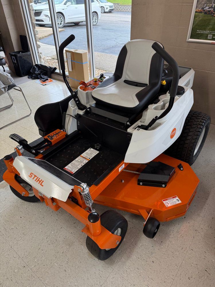 Orange and white Stihl zero-turn lawn mower on display inside a showroom, with a black seat and controls.