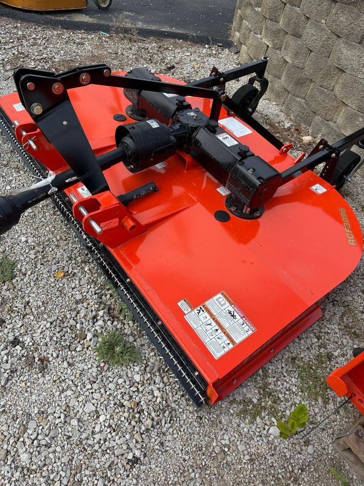 Orange rotary mower on gravel. Black blades and PTO shaft.
