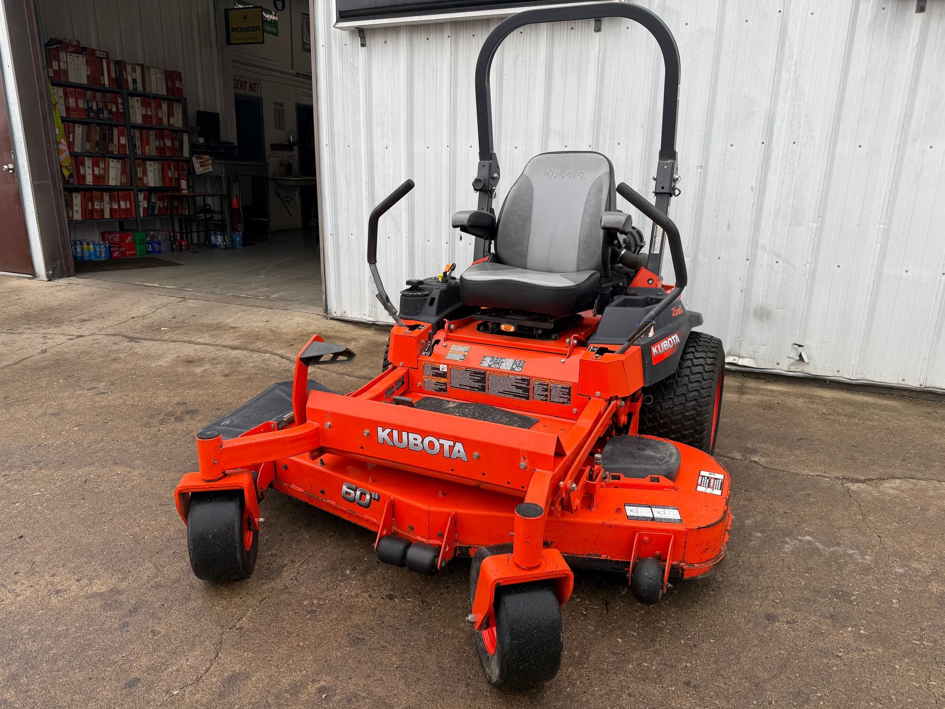 Orange tractor with front loader and backhoe parked in front of a building with a "Dixie Chopper" sign.