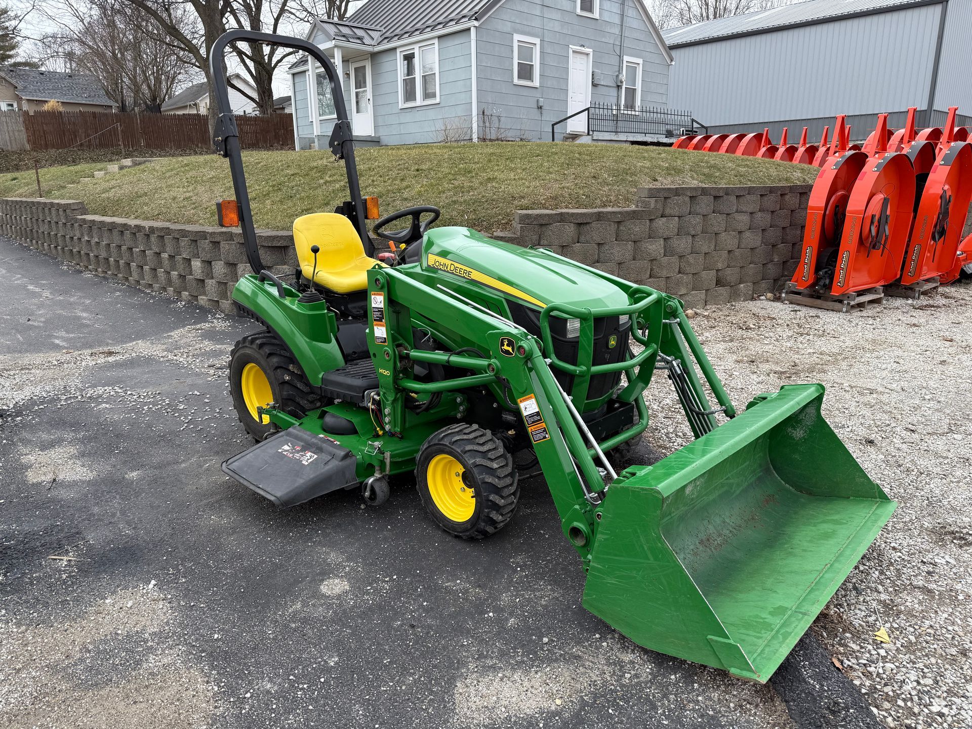 Orange tractor with front loader and backhoe parked in front of a building with a "Dixie Chopper" sign.