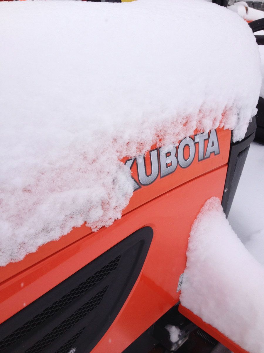 Orange Kubota tractor covered in snow.