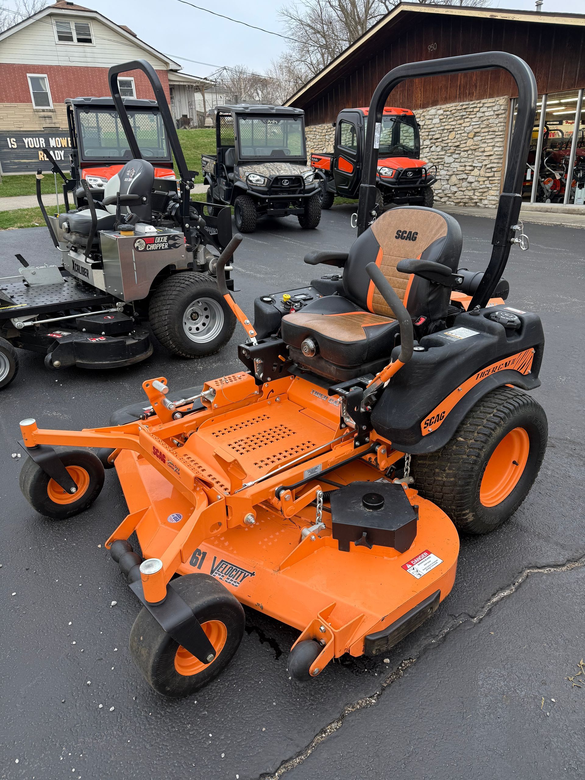Orange tractor with front loader and backhoe parked in front of a building with a "Dixie Chopper" sign.