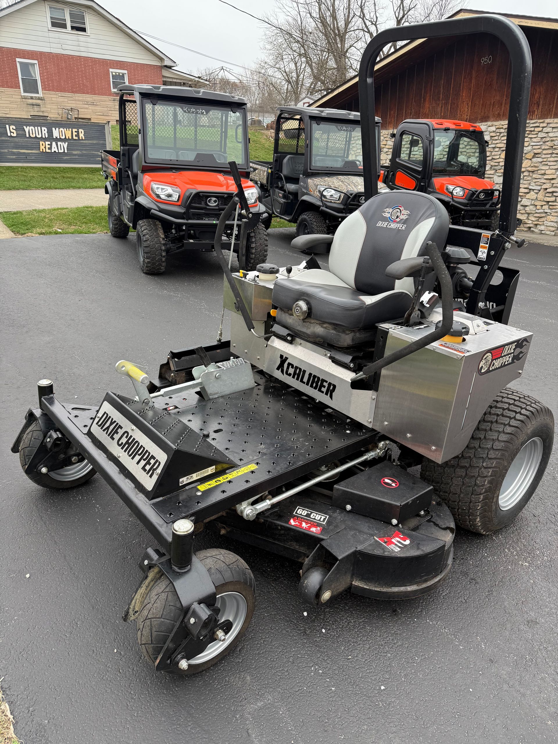 Orange tractor with front loader and backhoe parked in front of a building with a "Dixie Chopper" sign.