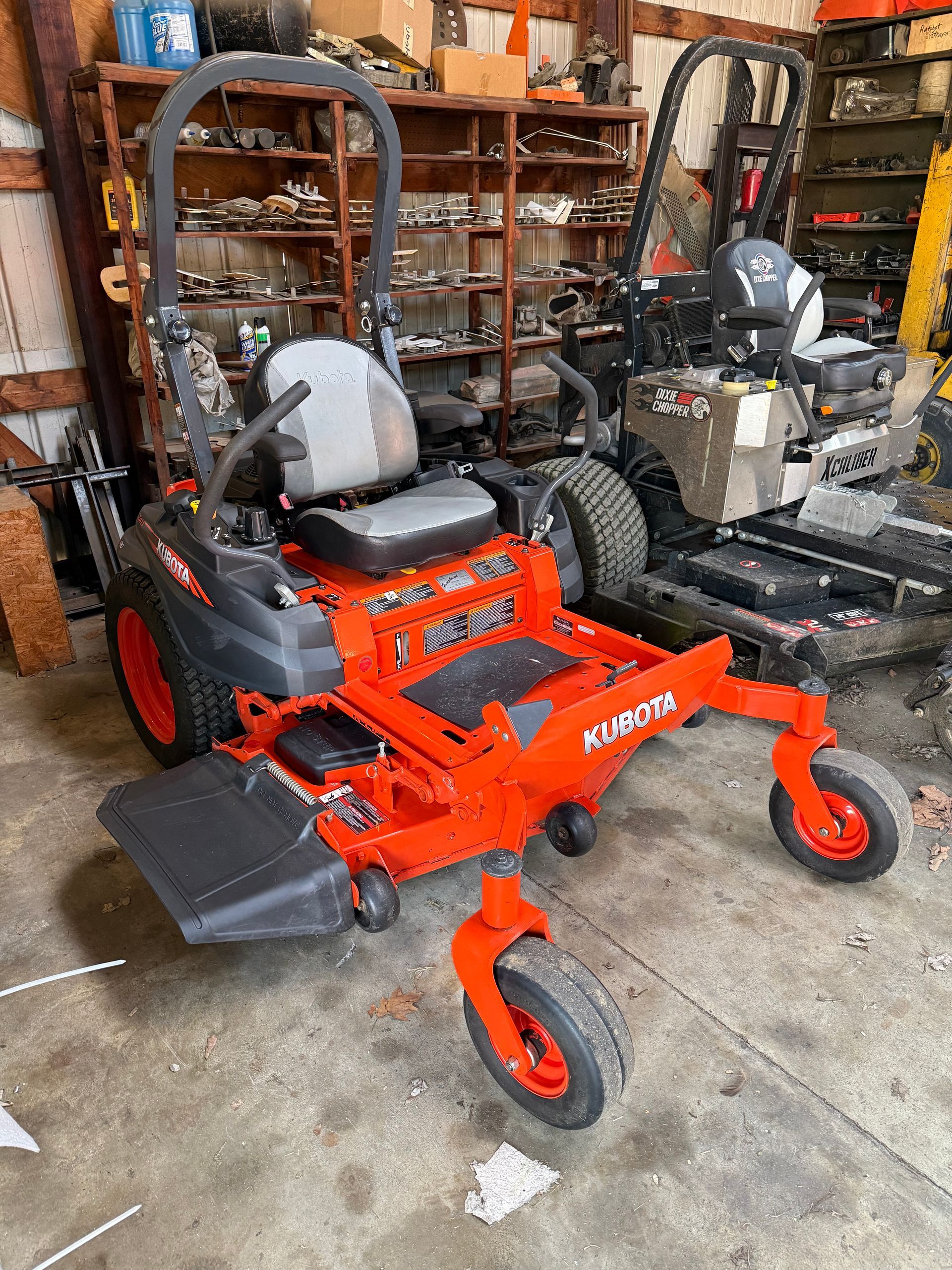 Orange tractor with front loader and backhoe parked in front of a building with a "Dixie Chopper" sign.
