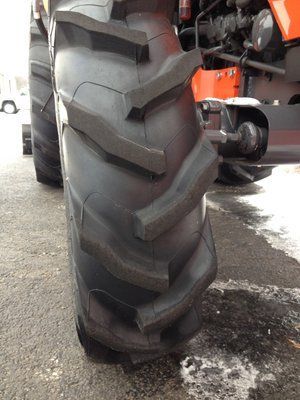 Black tractor tire with large tread pattern on a wet surface.
