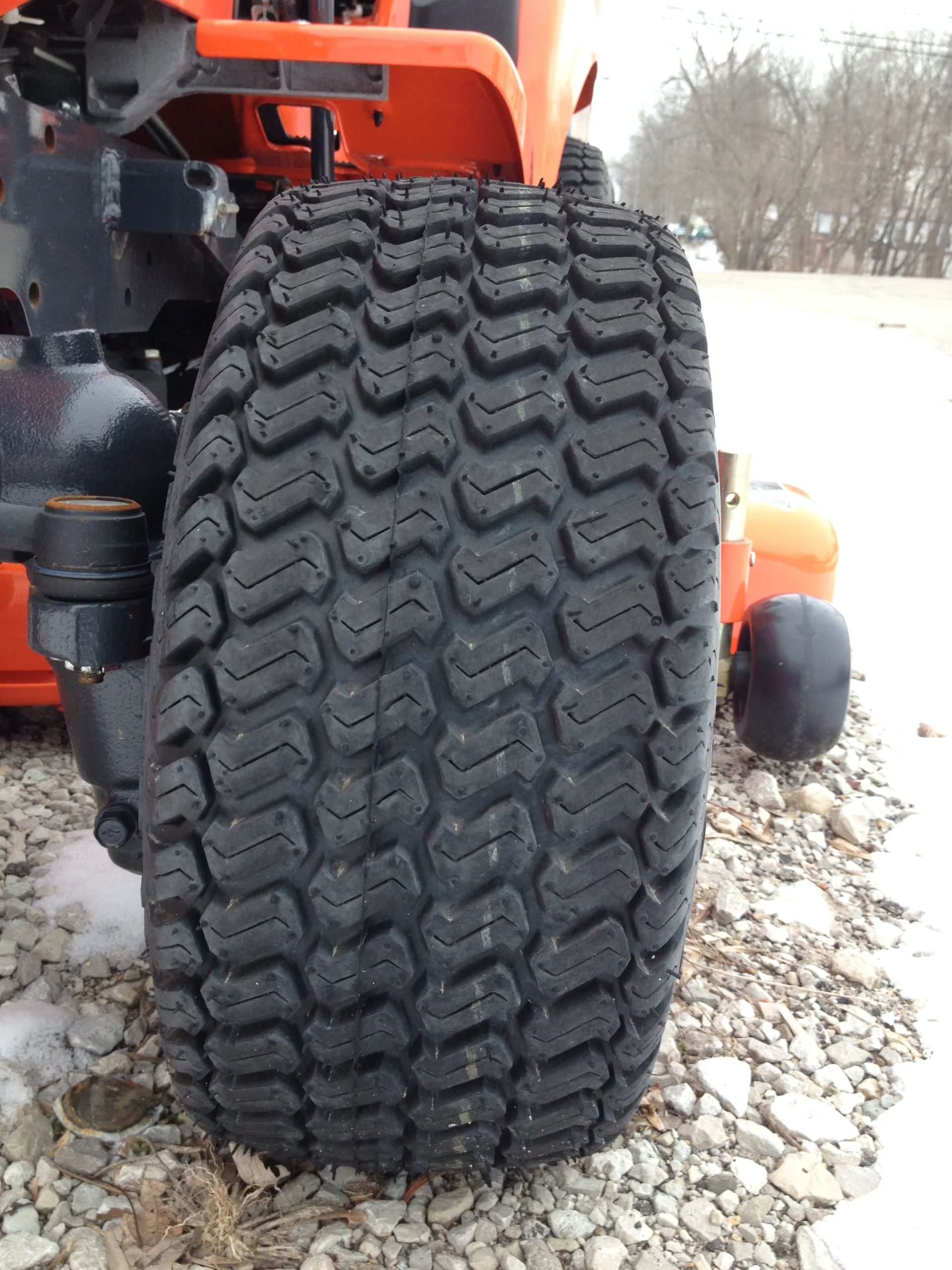 Close-up of a large, black tractor tire on a lawn mower, orange and black machinery visible.