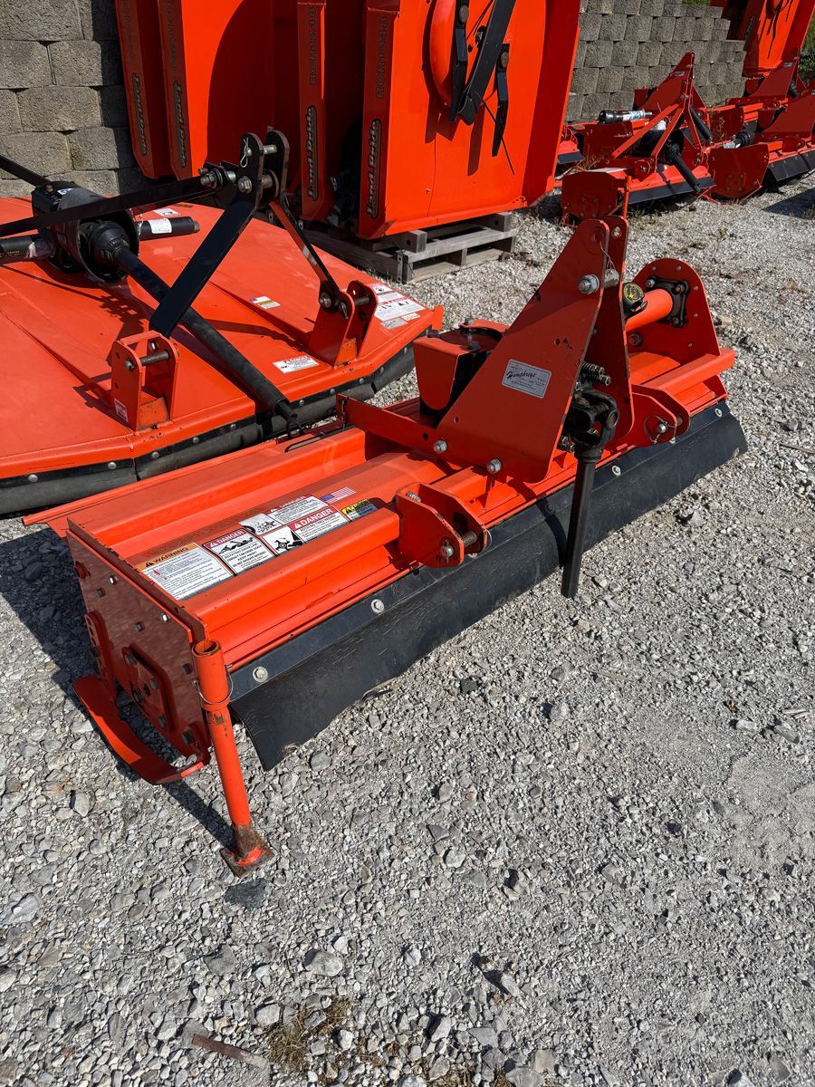 Orange rotary mower attachment on gravel, with another orange machine in the background.