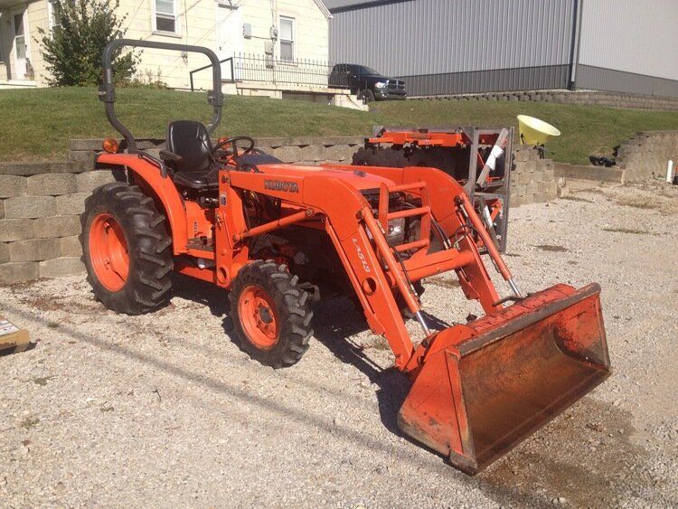 Orange Kubota tractor with a front-end loader on gravel in front of a building.