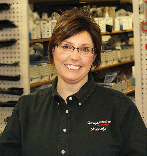 Woman in glasses, dark green shirt, smiling in hardware store, logo visible.