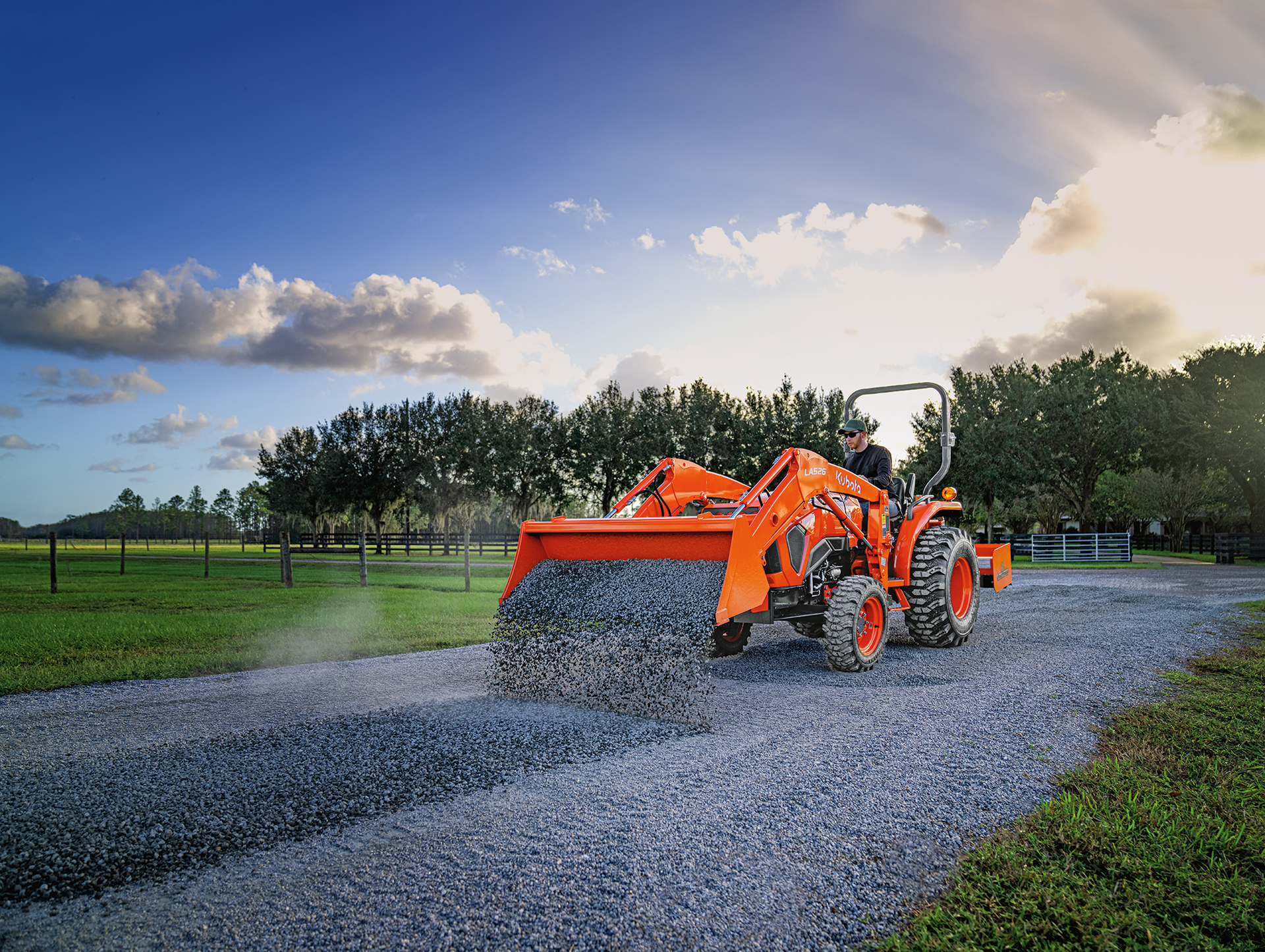 Orange tractor grading a gravel road on a sunny day.