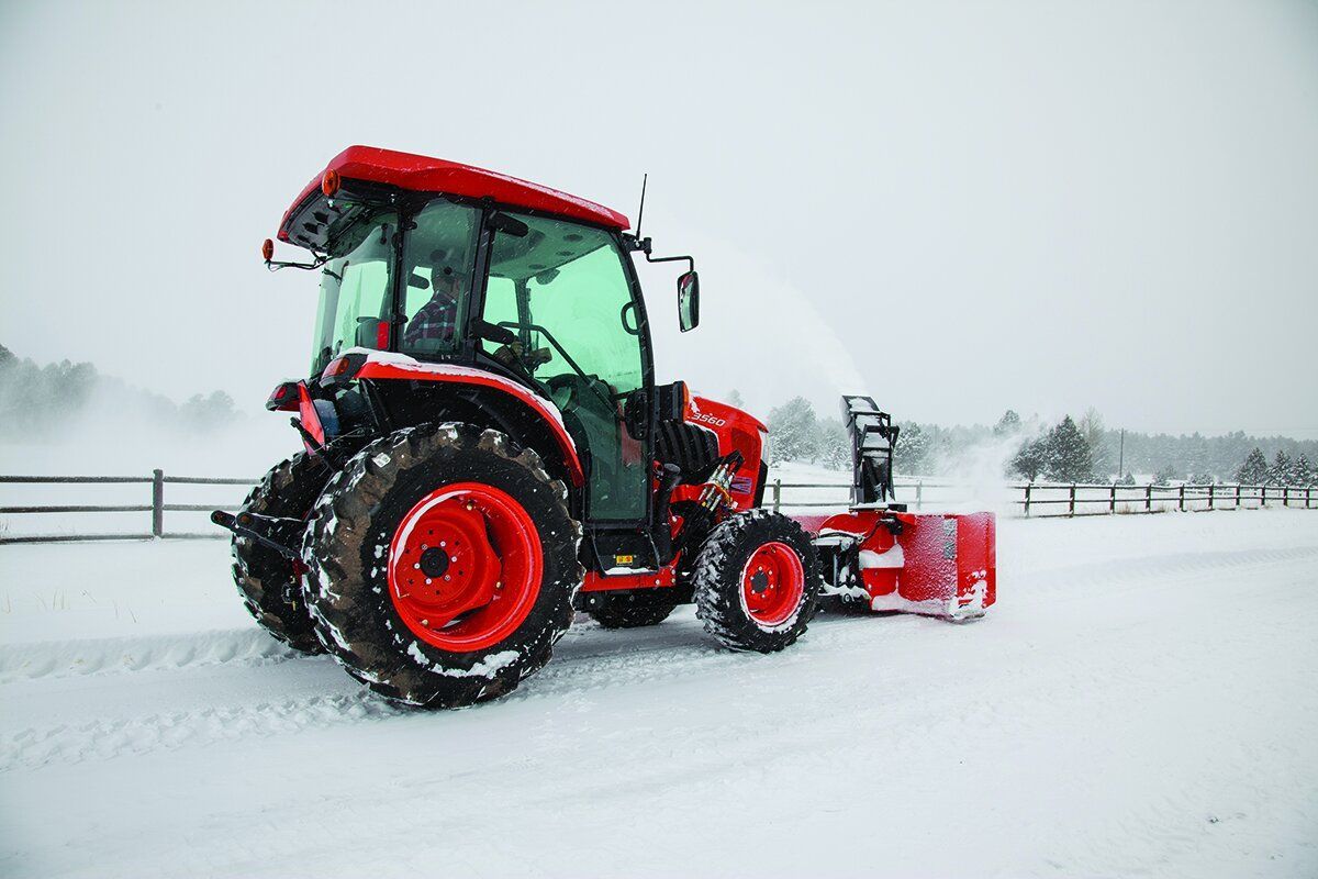 Red tractor plowing snow with snow blower in a snowy field.
