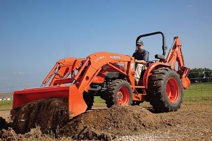 Orange tractor with a person in the driver's seat leveling soil in a field. Blue sky.