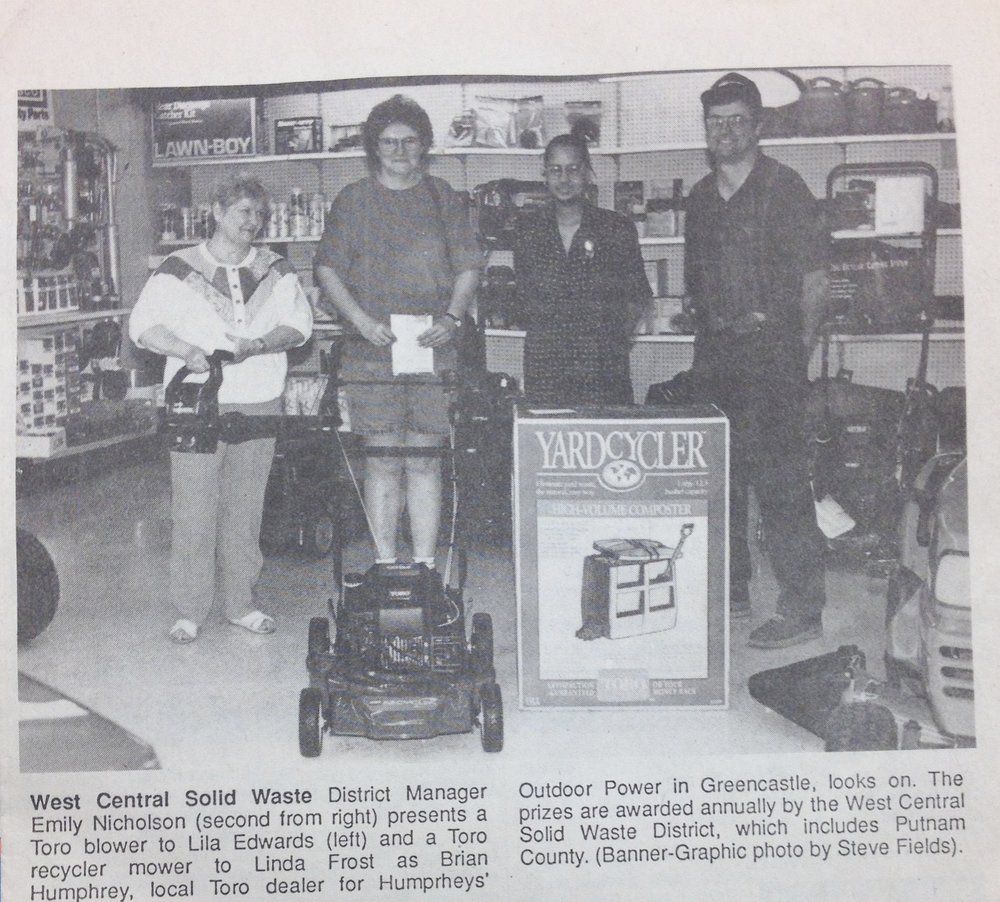 People pose with lawnmower and YardCycler box in a store.