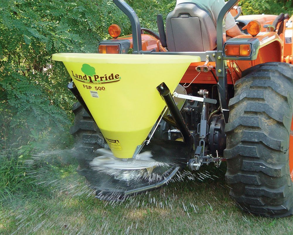 Yellow Land Pride spreader dispensing material from tractor.