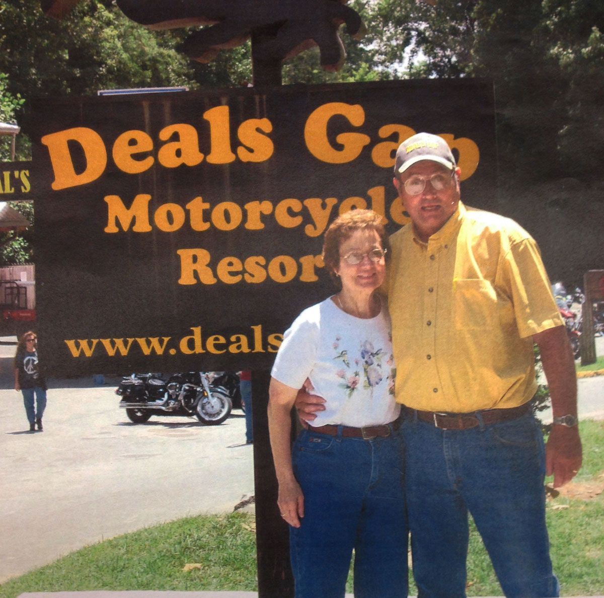 Couple posing at Deals Gap Motorcycle Resort sign. Man in yellow shirt, woman in white top.