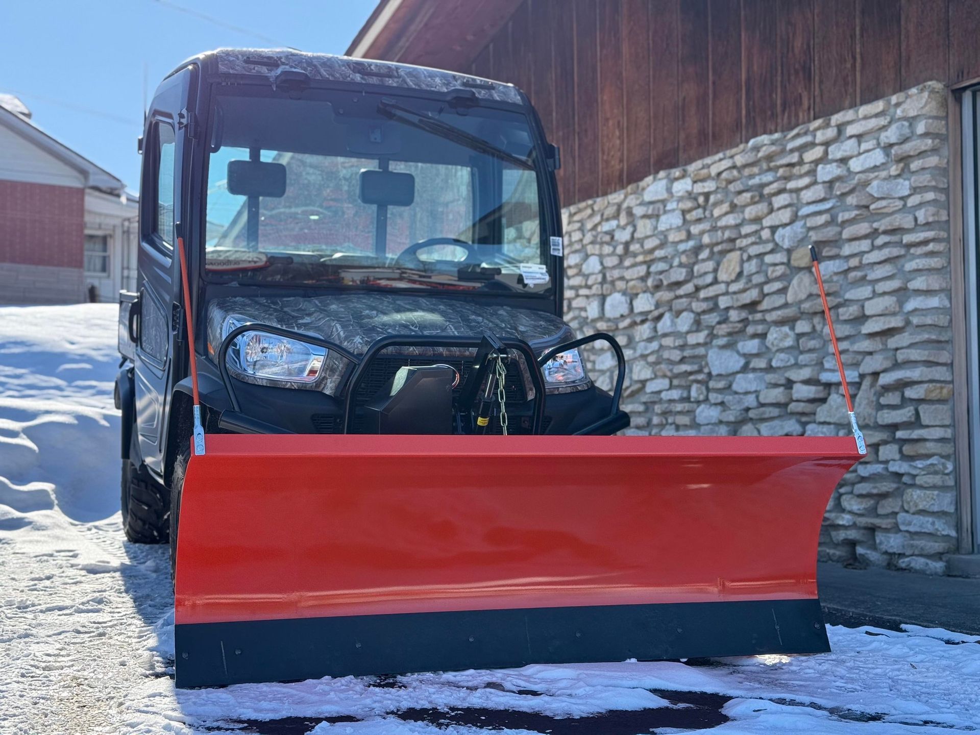 Black utility vehicle with orange snowplow in front of a building covered in snow.