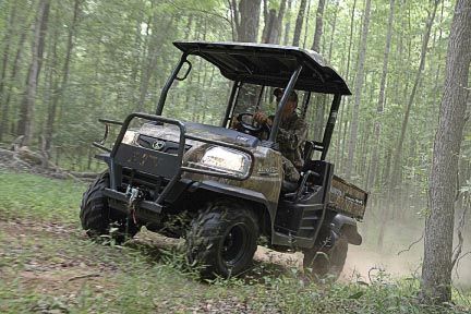 Dark green UTV driving uphill through a wooded area; driver visible.