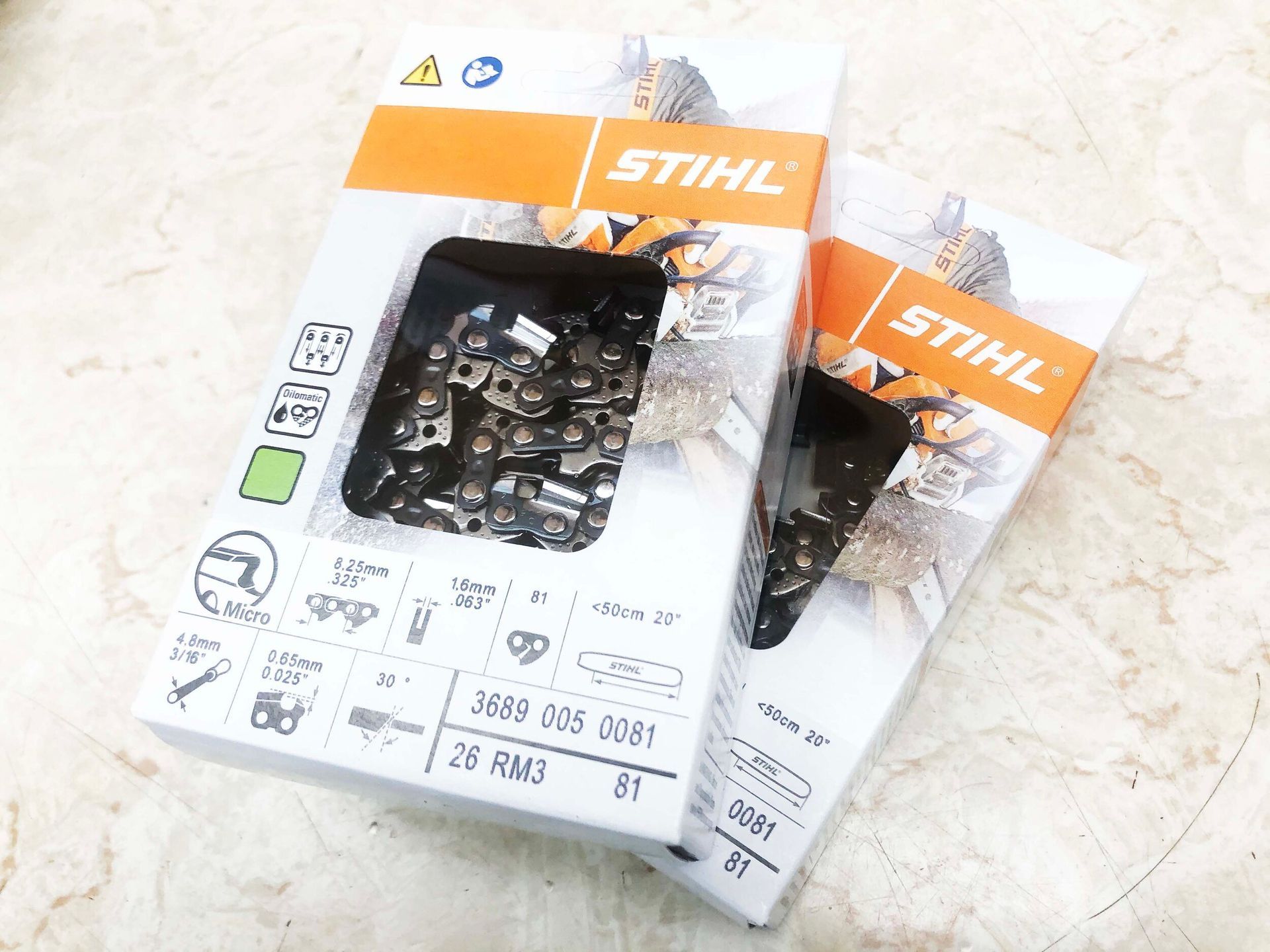 Two Stihl chainsaw chain boxes, white and orange, on a light-colored surface. One box has a visible chain.