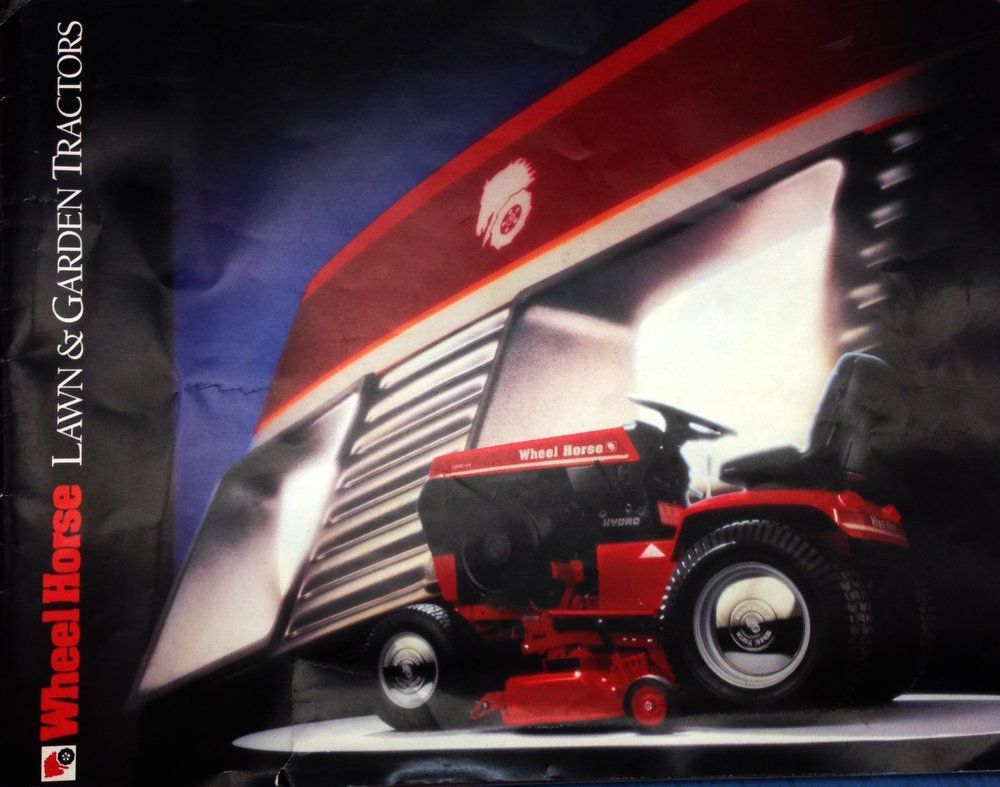 Red Wheel Horse lawn tractor parked in front of a red building with the Wheel Horse logo.