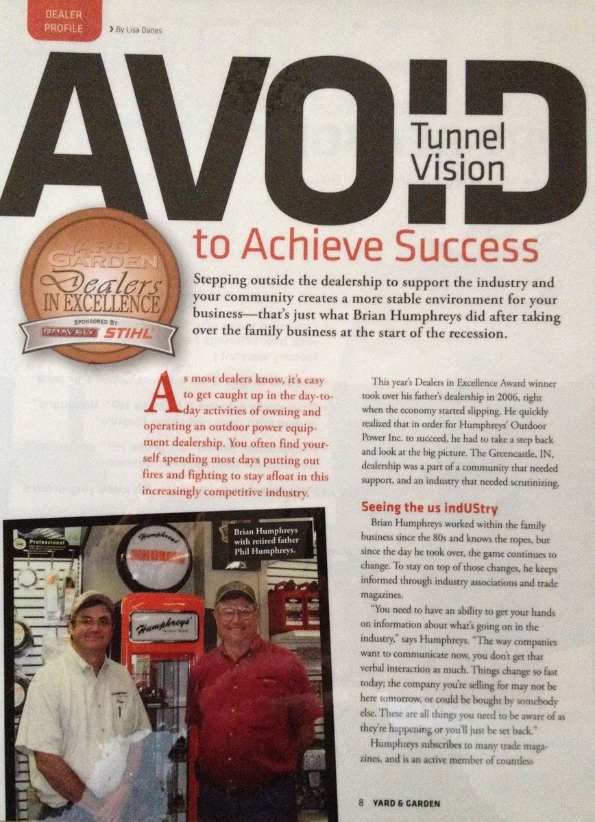 Three people standing with a lawnmower inside a building. Two men and one woman.
